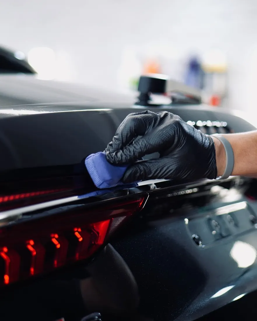Recubrimiento cerámico para autos: aplicación de recubrimiento cerámico con aplicador azul en la cajuela de un auto negro