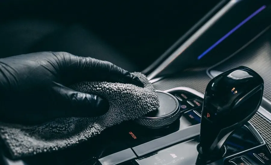 Lavado de interiores de autos: limpieza de la consola central con microfibra gris y guante negro