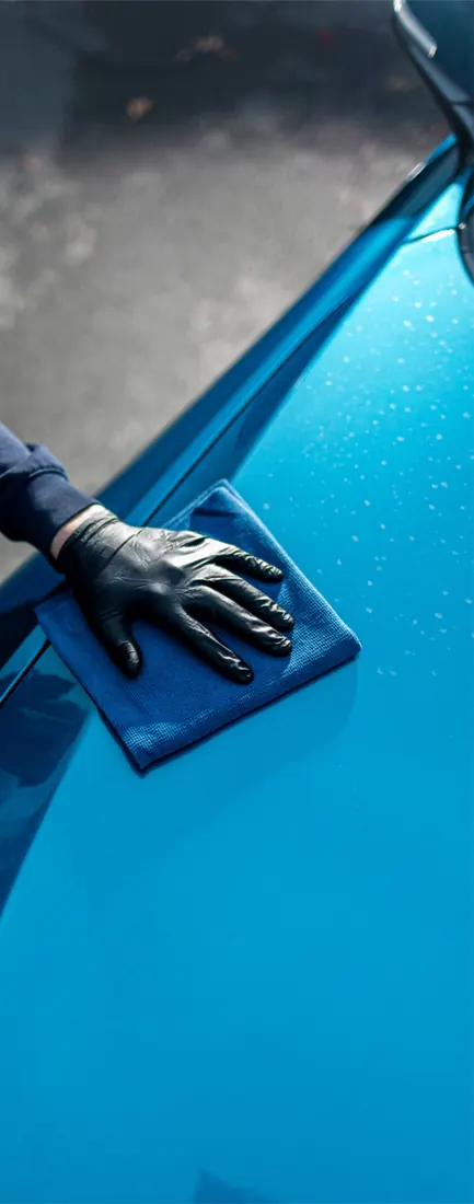 Protección acrílica para autos: microfibra azul sobre un cofre turquesa con gotas de agua
