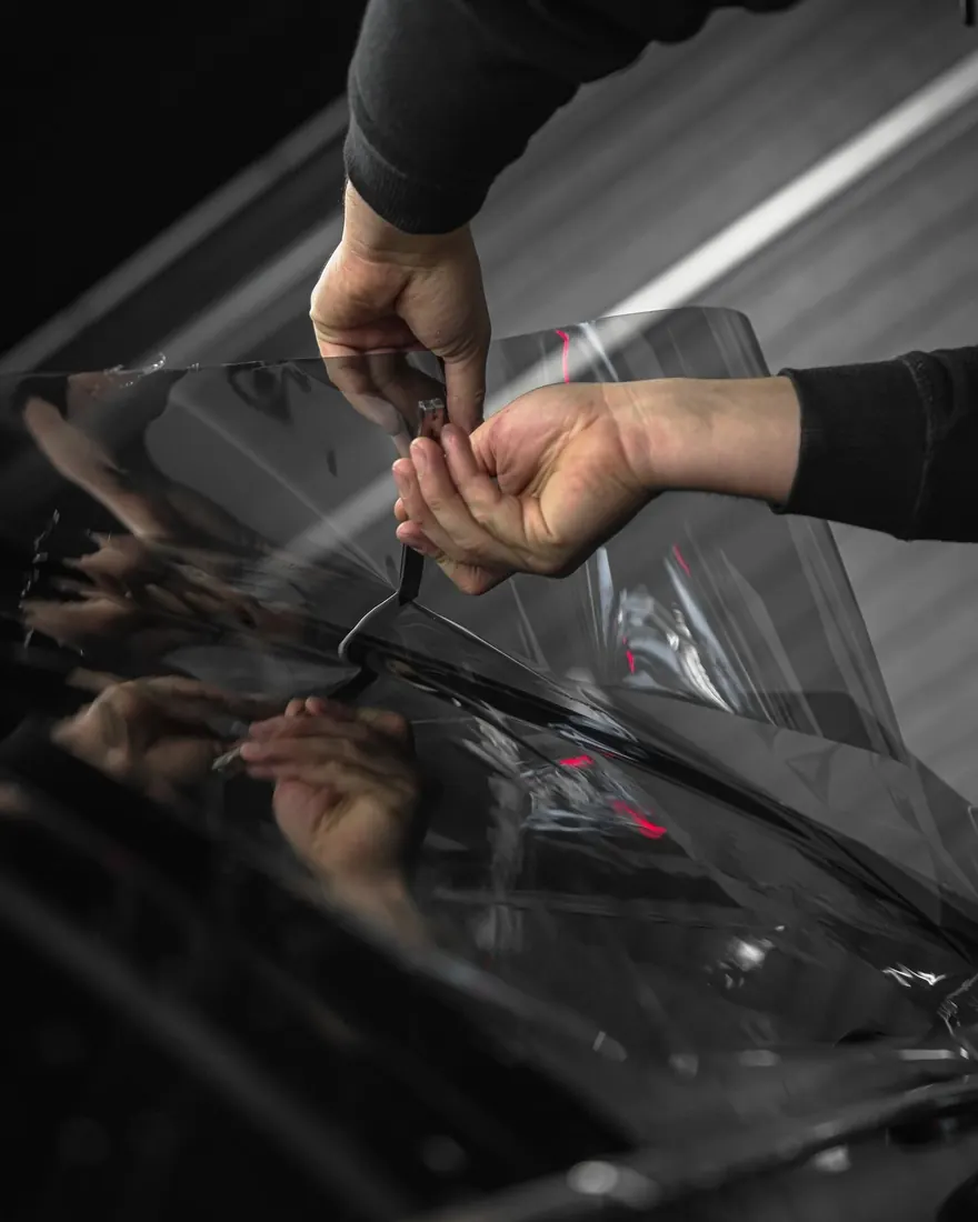 Ppf autos: manos colocando película PPF transparente sobre un auto negro