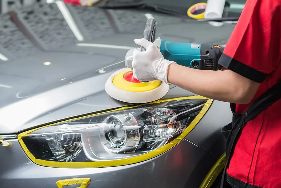 Blog de detallado automotriz: faros de coche opacos - detallador puliendo un faro con máquina y cinta de enmascarar sobre un auto gris